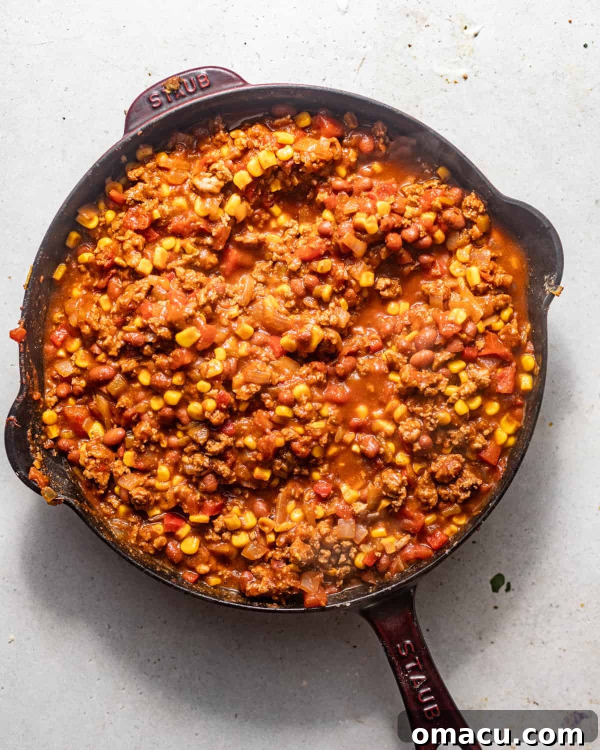 Ground beef, seasoning, onion, bell pepper, Rotel, corn, and chili beans are cooked together in a large skillet, bubbling with rich flavors.