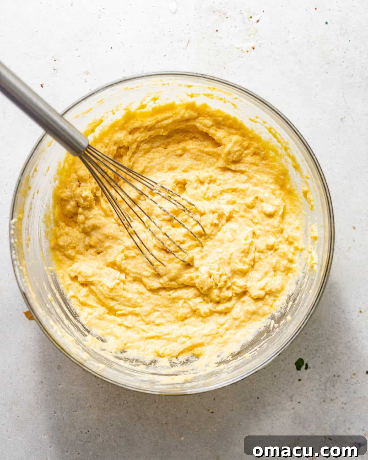 Cornbread batter is whisked together smoothly in a large mixing bowl, ready for the casserole.