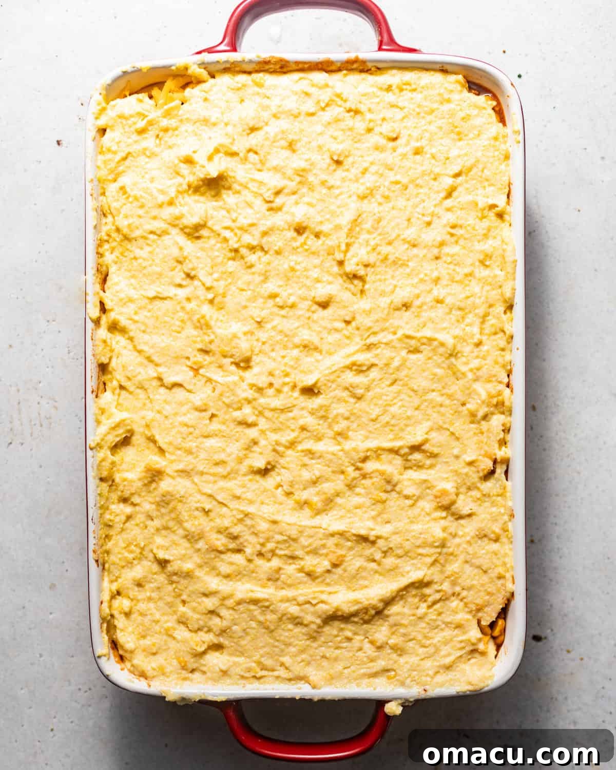 The cornbread cowboy casserole in a baking dish, with the cornbread batter spread smoothly over the ground beef and cheese layers.