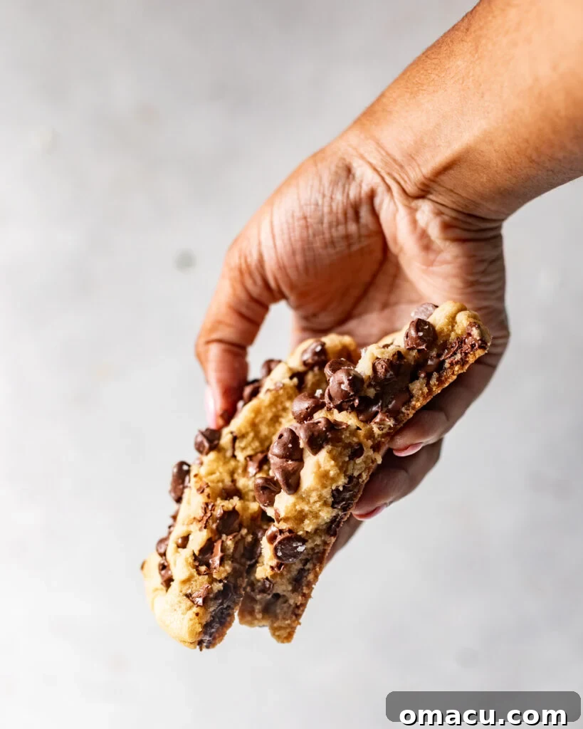 A chocolate chip cookie broken in half, revealing a gooey, melty chocolate center, held by a hand.