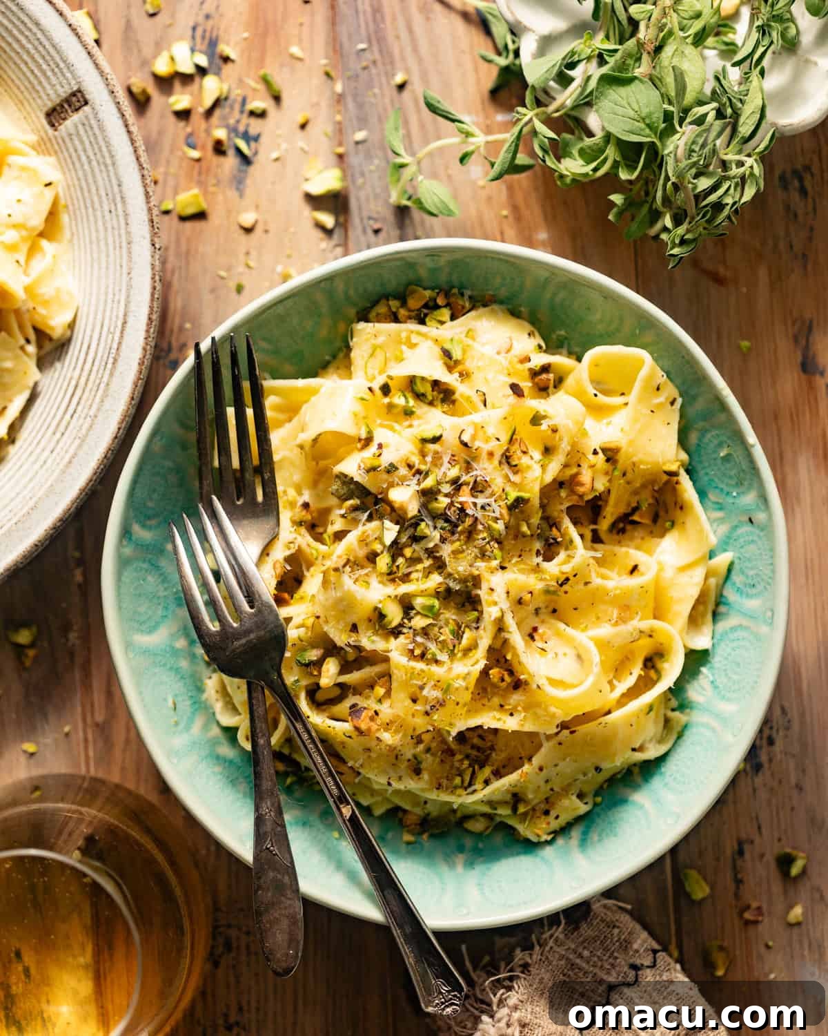 A vibrant blue bowl filled with lemon caper pasta, garnished with fresh parsley, chopped pistachios, and grated Parmesan cheese.