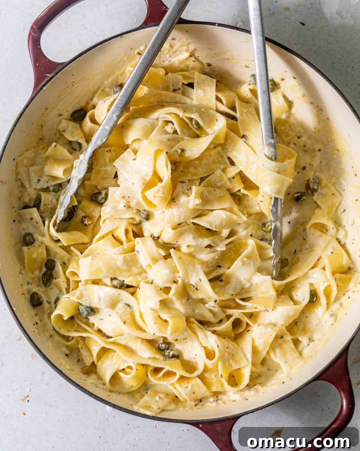 Pasta noodles glistening in the creamy lemon caper sauce in a large skillet, perfectly coated.