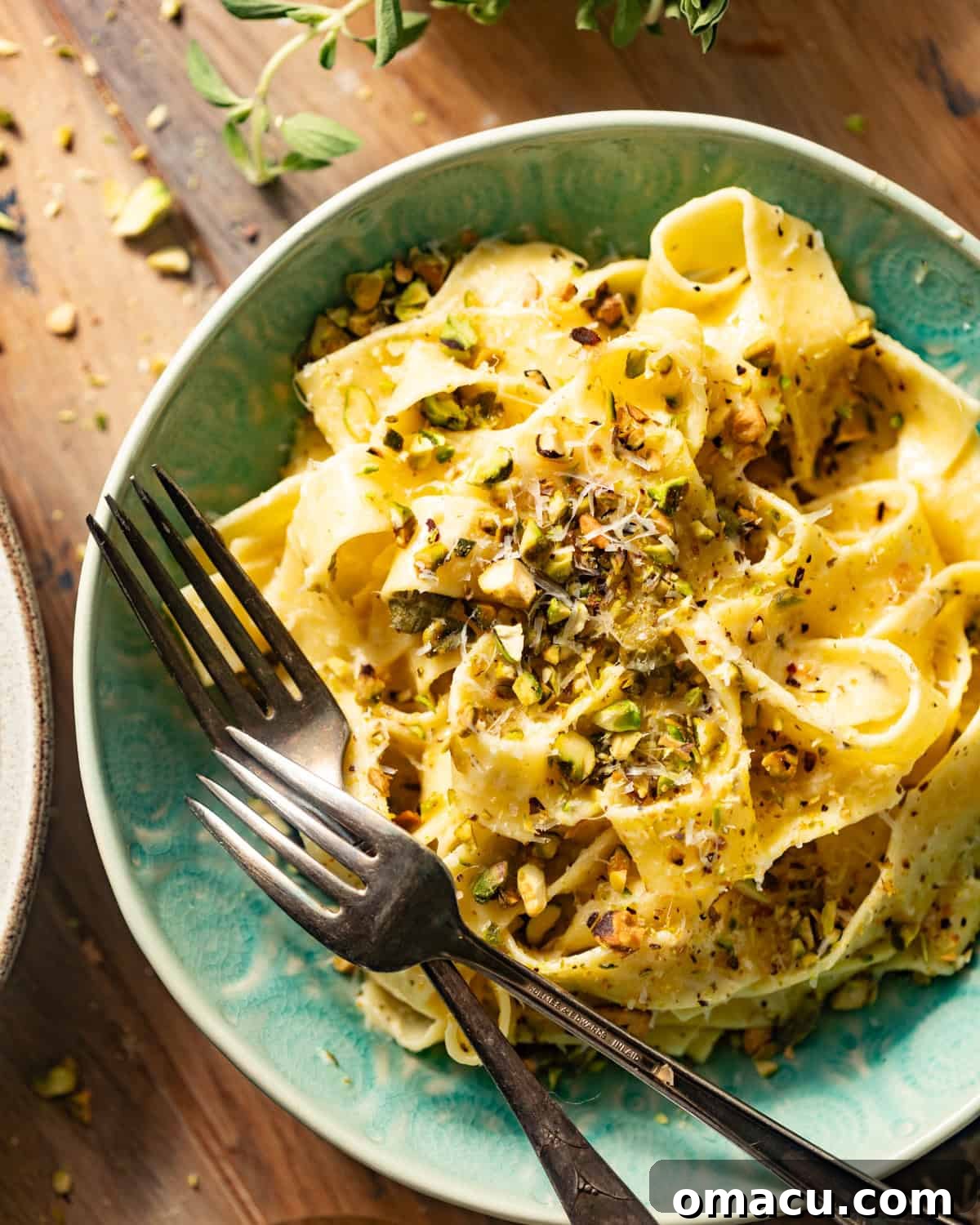 Two forks dipped into a bowl of lemon caper pasta, highlighting its appetizing creamy texture and garnishes.