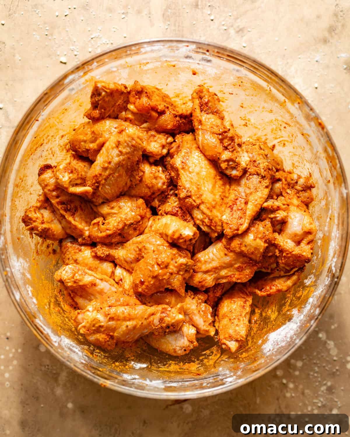 Chicken wings in a large bowl, thoroughly coated in seasoning mixture.