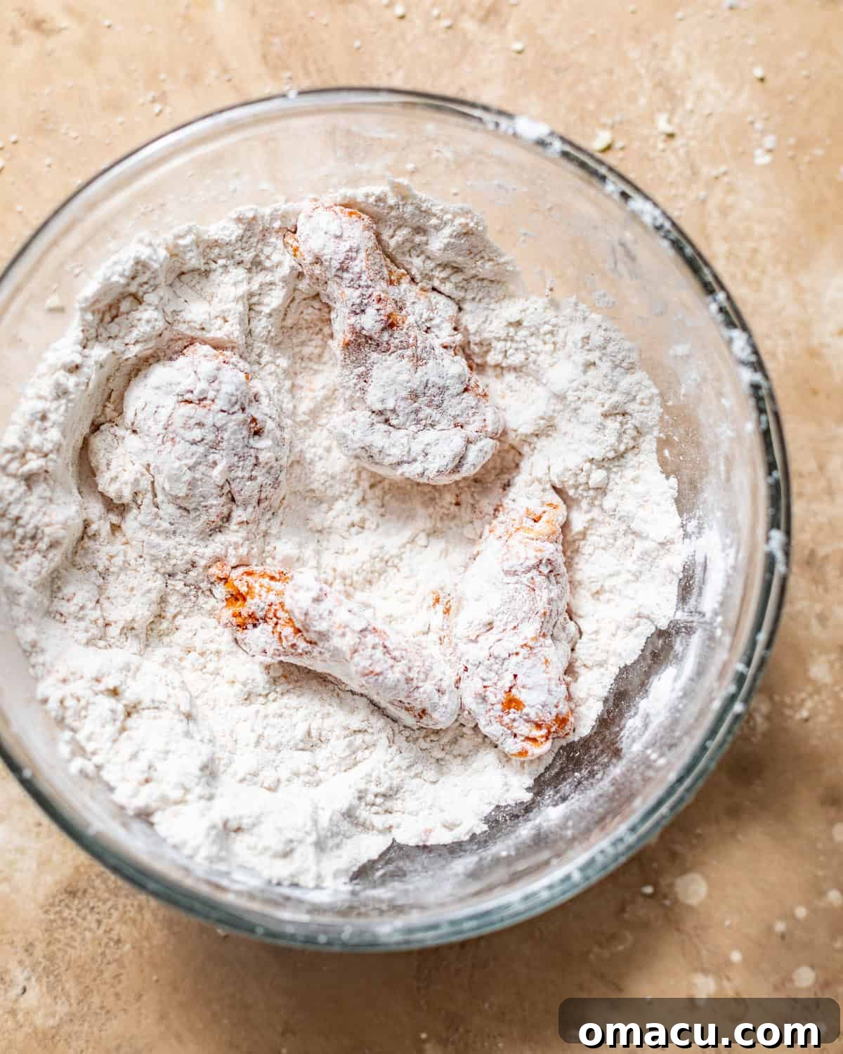 Chicken wings thoroughly coated in a seasoned flour mixture in a bowl.