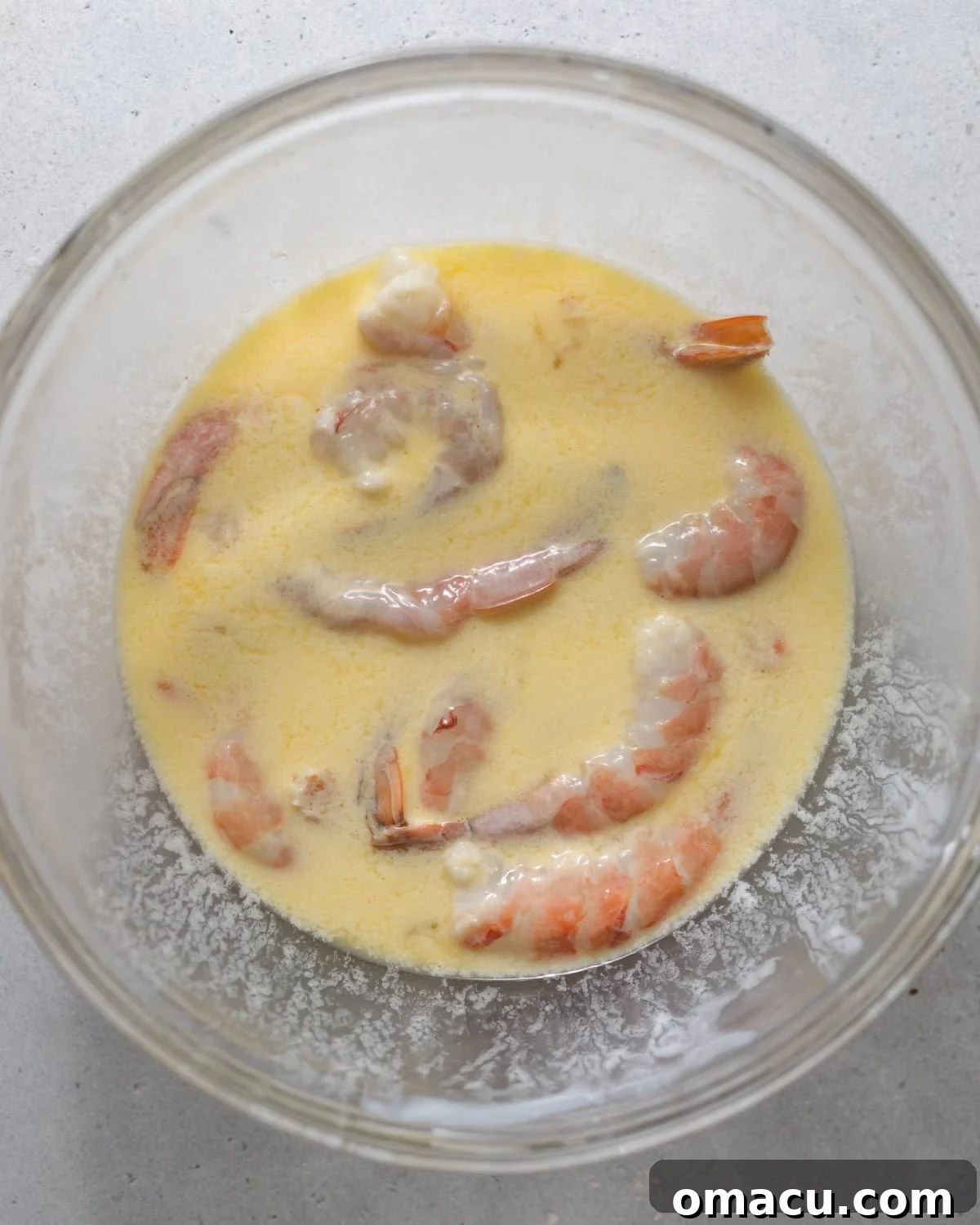 Shrimp soaking in a bowl of buttermilk, eggs, and cajun seasoning.