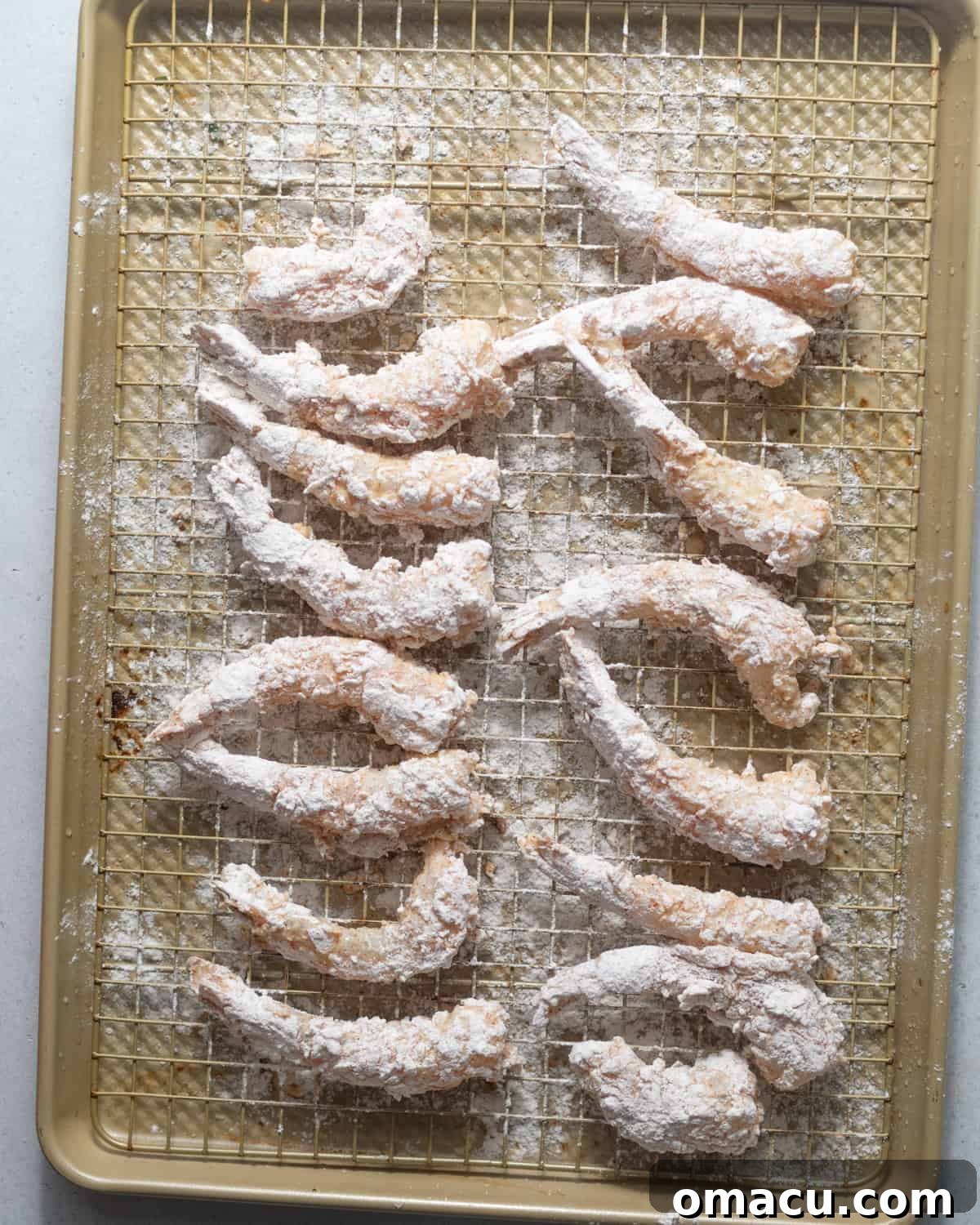 Battered shrimp resting on a wire rack before frying.