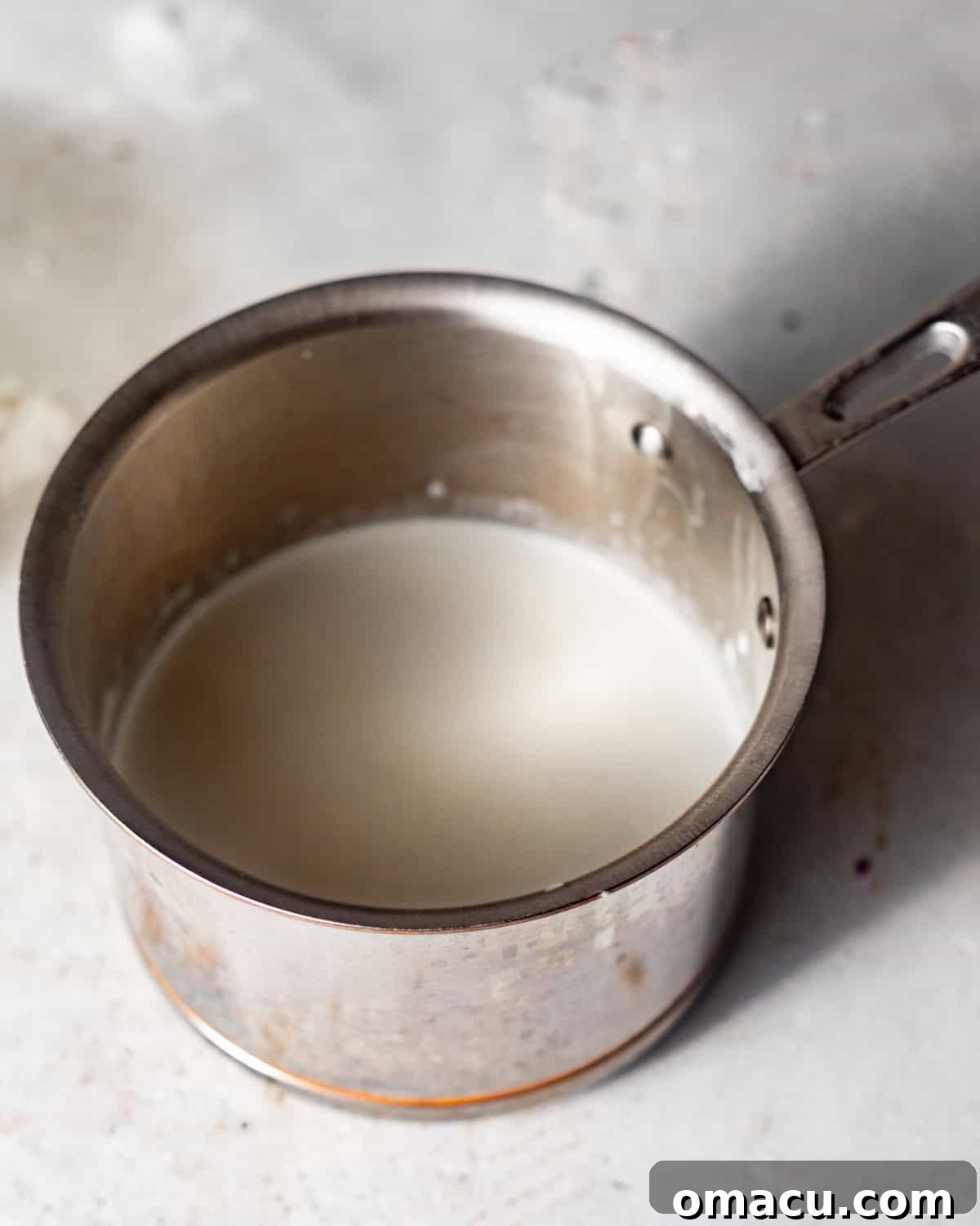 Heavy cream and whole milk gently warming in a small saucepan on a stovetop, preparing for the rich custard base.