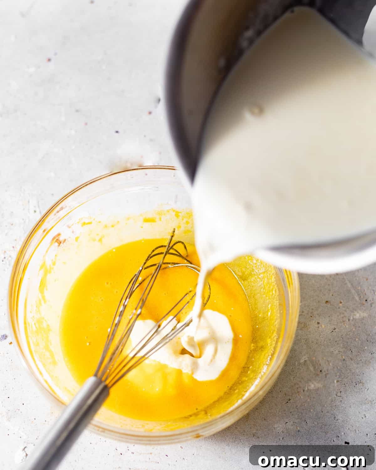 Gently pouring warmed heavy cream into the whisked egg yolk and sugar mixture, carefully tempering the eggs to prevent scrambling.