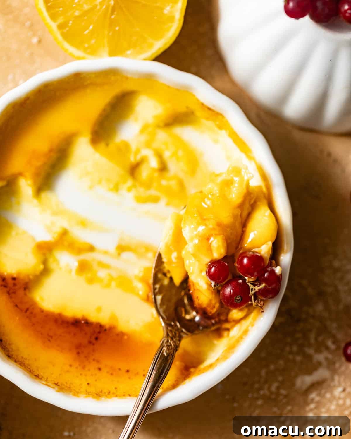 A small spoon poised in a ramekin of lemon creme brulee, about to scoop a mouthful of the creamy, caramelized dessert.