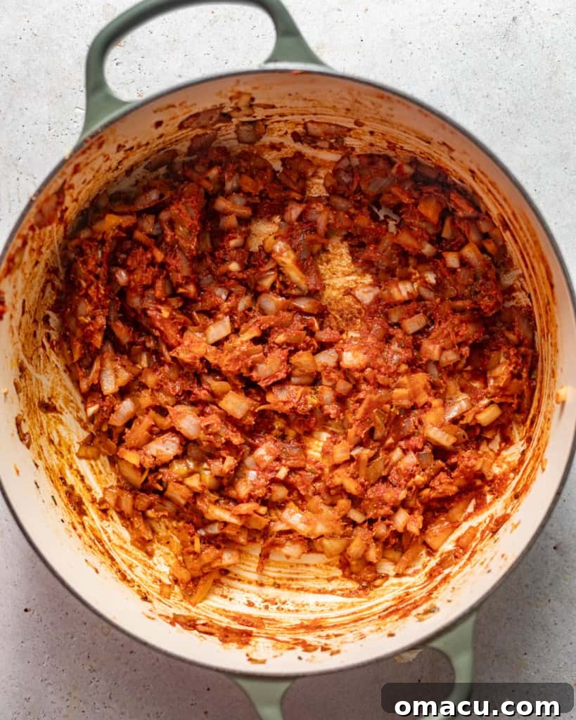 Sautéed onions, garlic, herbs, tomato paste, and diced tomatoes simmering together in a pot.