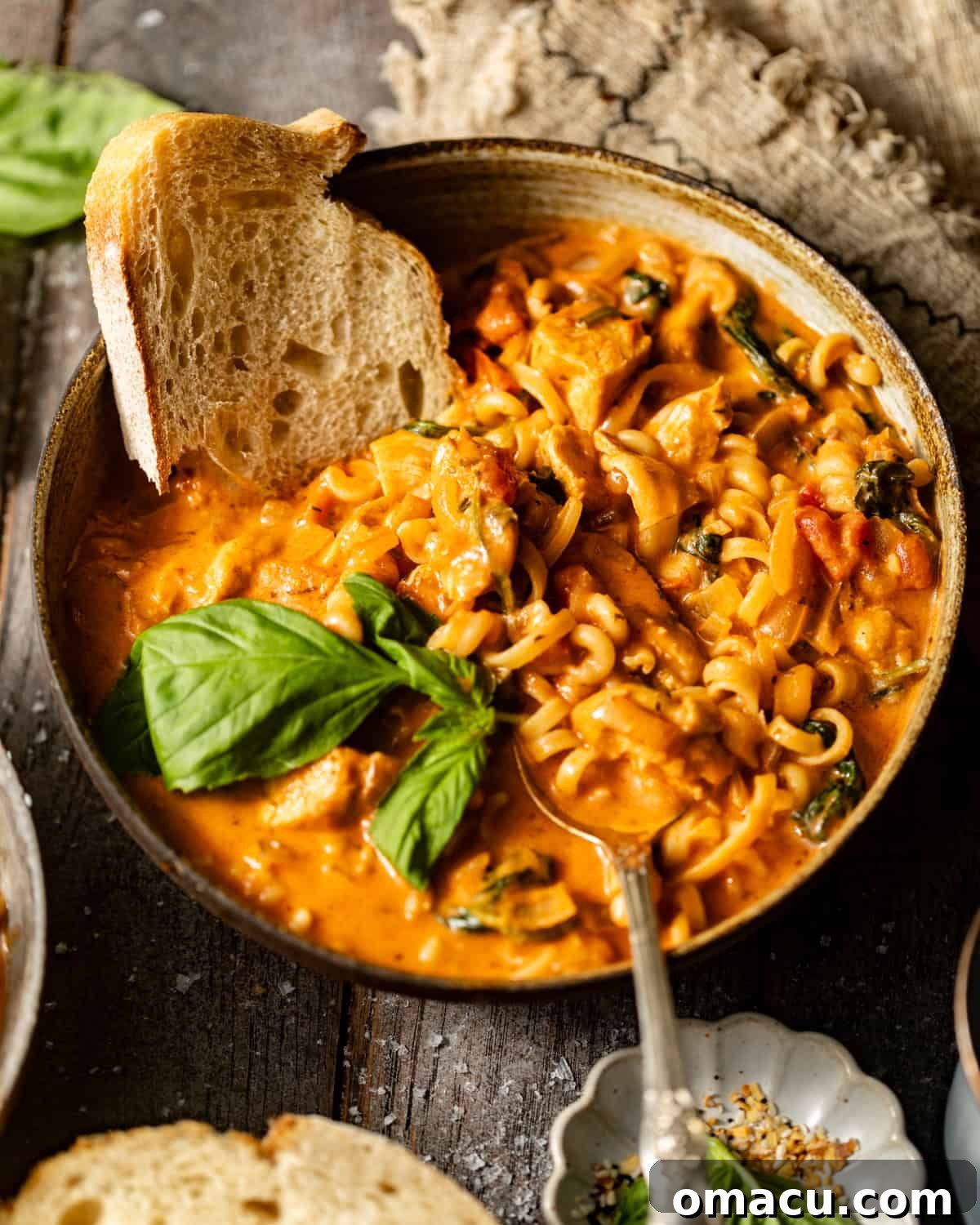 A prepared bowl of Marry Me Chicken Soup served with crusty bread and fresh basil garnish.