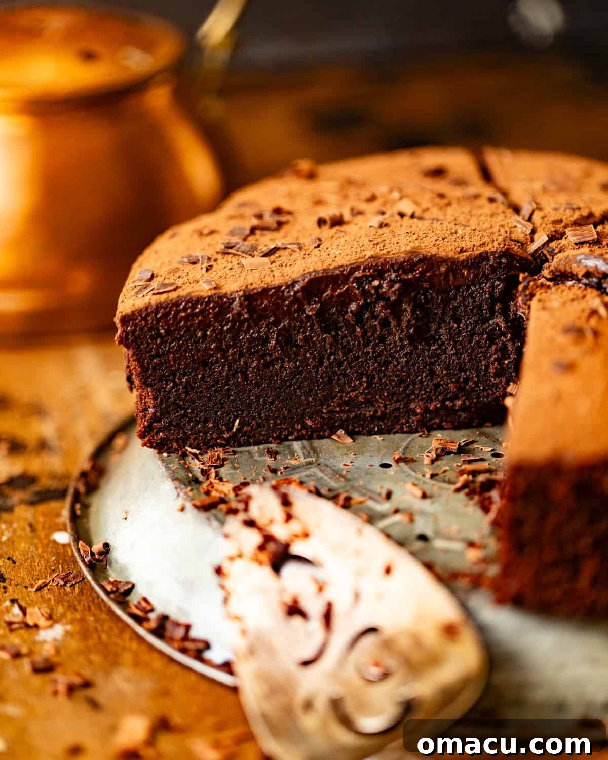 Sliced chocolate mud cake on a pie plate topped with chocolate ganache and a dusting of cocoa powder.