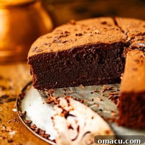 Sliced chocolate mud cake on a pie plate topped with chocolate ganache and a dusting of cocoa powder.