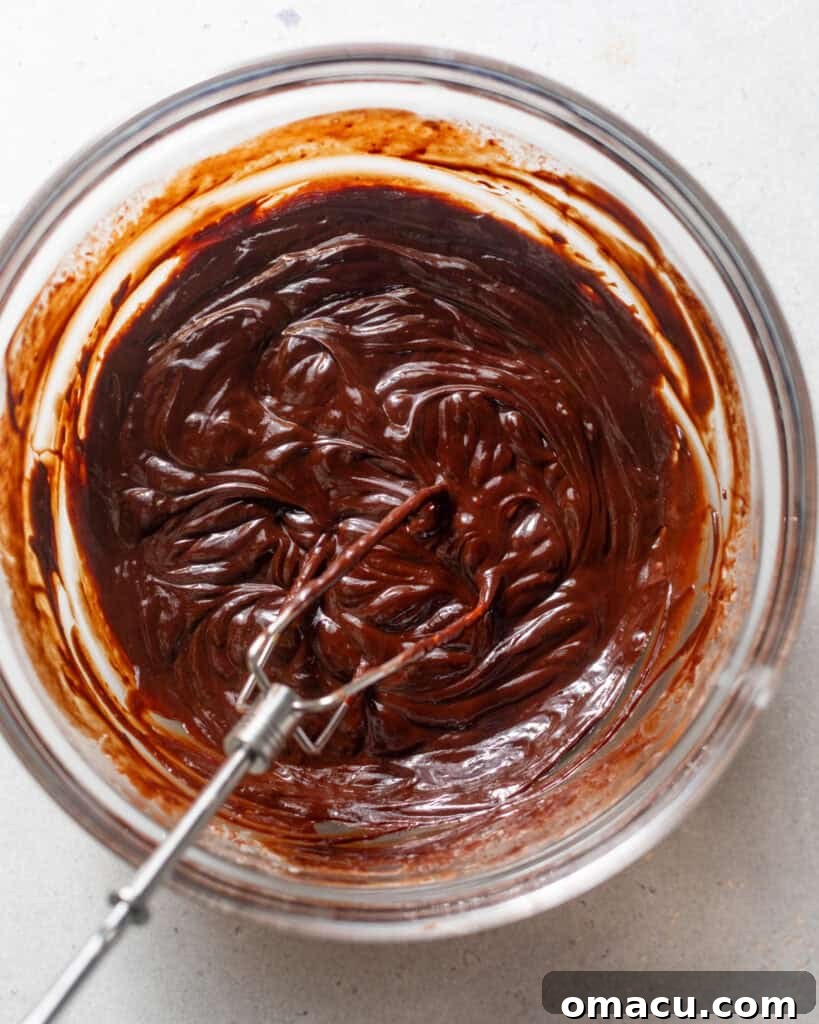 Chocolate ganache in a mixing bowl with a whisk, showing its smooth, glossy texture.