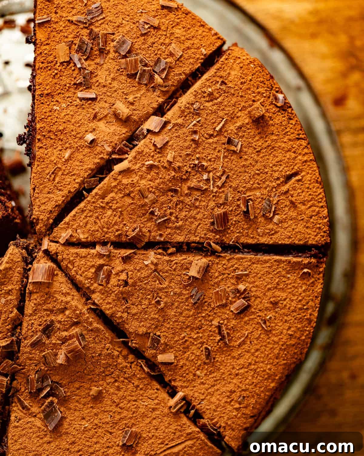 Sliced chocolate mud cake with cocoa powder and chocolate shavings on top, after ganache has set.