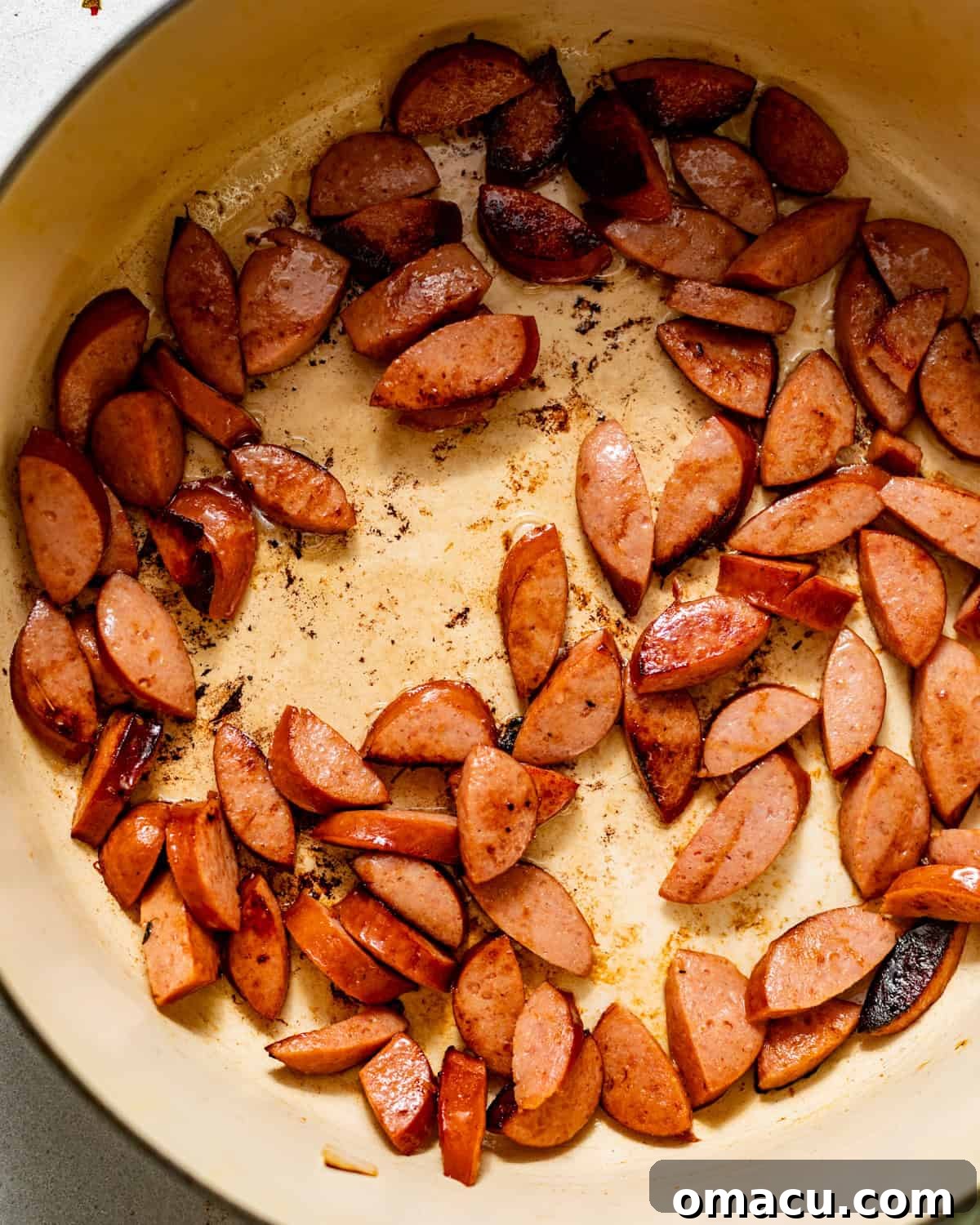 Browned slices of Andouille sausage cooking in a large pot with a small amount of olive oil.