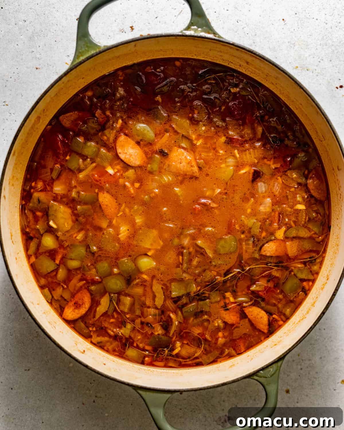 All gumbo base ingredients, including stocks, thyme, and returned sausage, simmering together in a large pot.