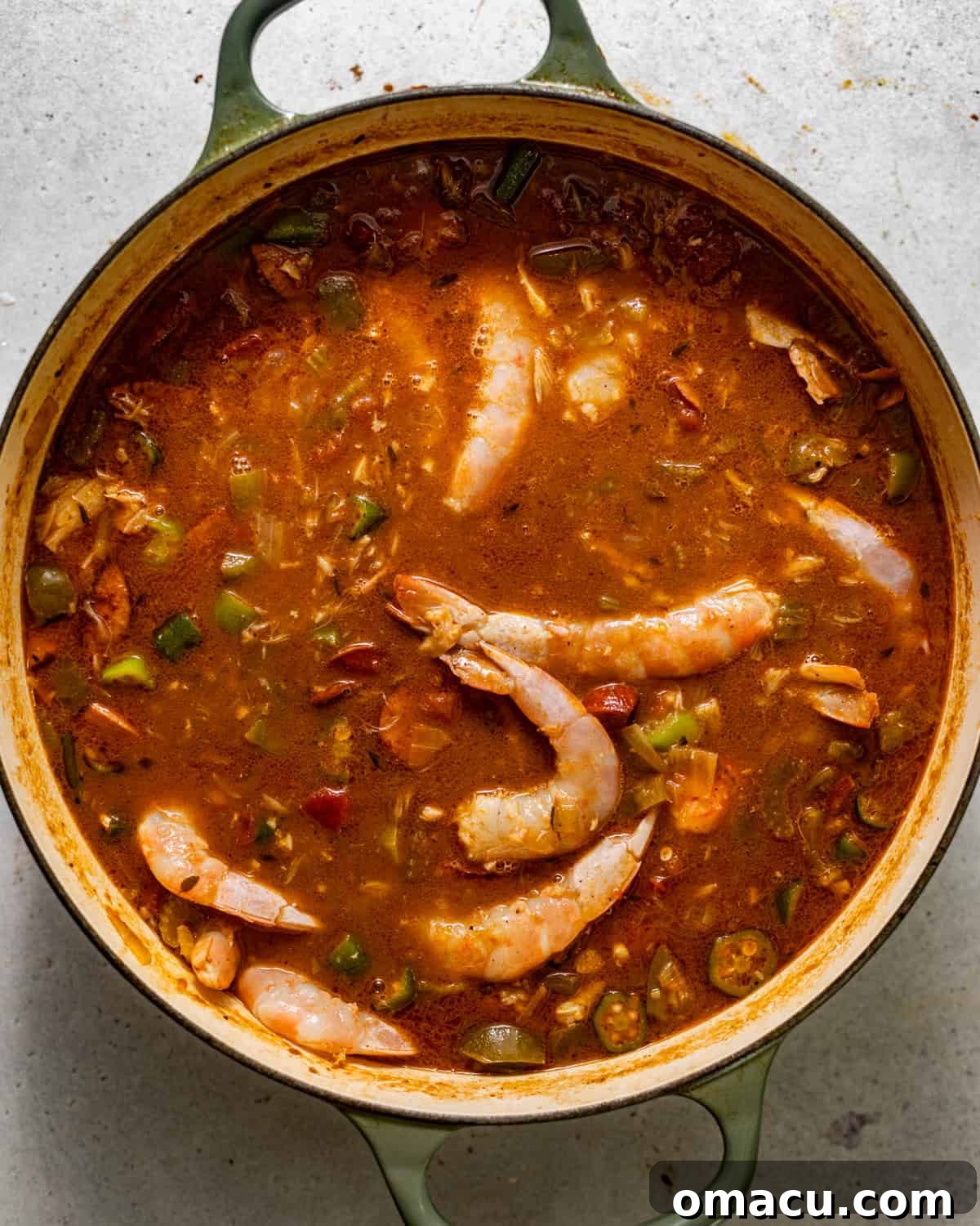 Shrimp and crab meat being added to the simmering gumbo in a large pot, ready for the final cooking stage.