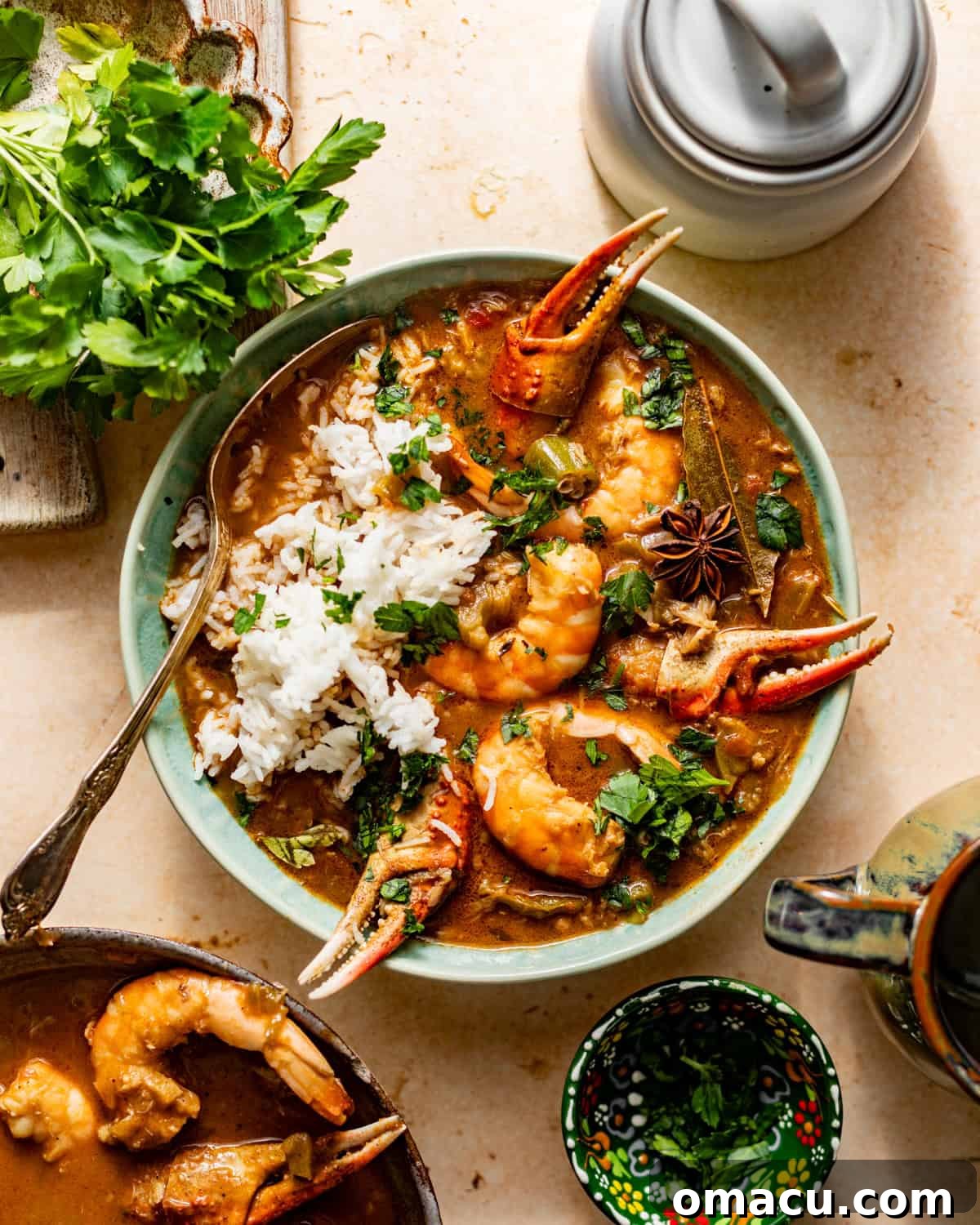 An overhead view of a bowl of Cajun seafood gumbo, generously topped with fresh parsley and served with a side of white rice and a spoon.