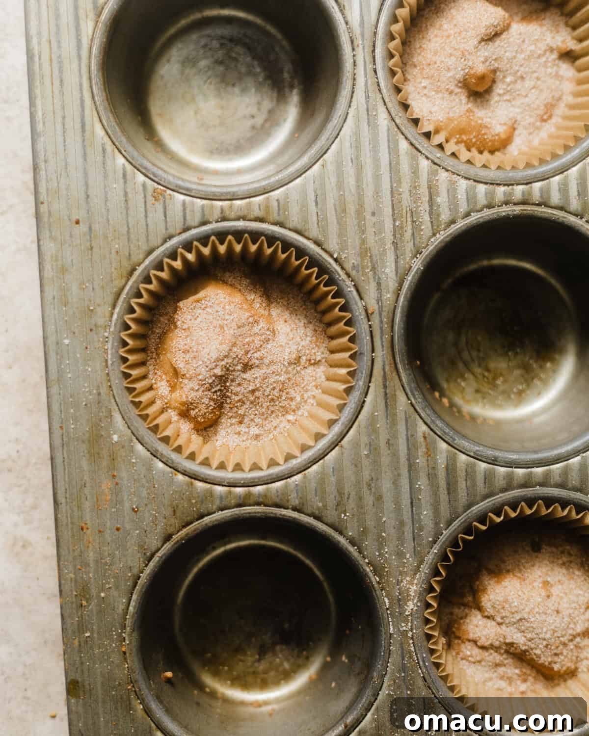 Coffee cake muffin batter in a muffin pan with cinnamon sugar sprinkled on top, ready for the next layer.