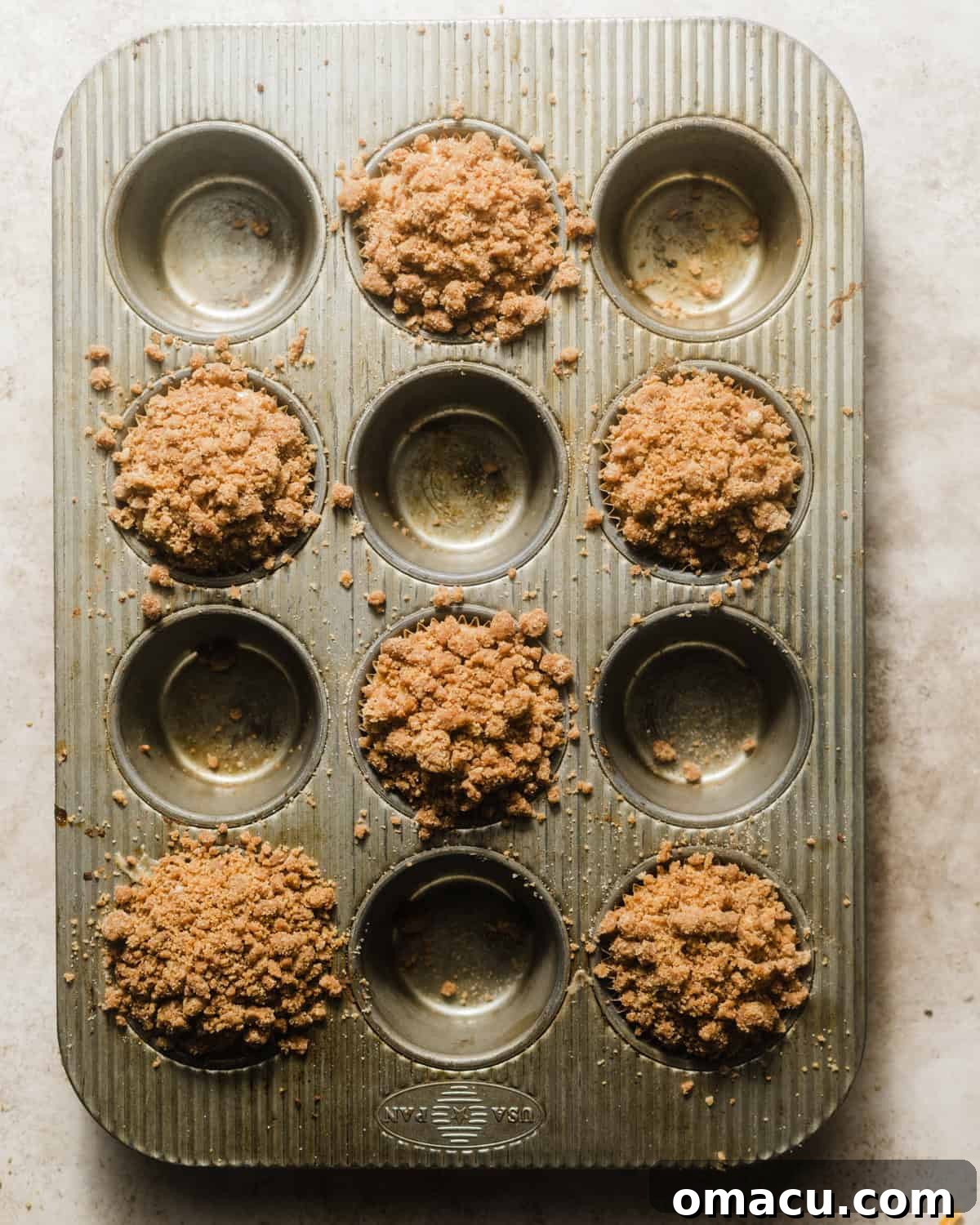 Assembled coffee cake muffins in a muffin pan with streusel topping, ready to bake.