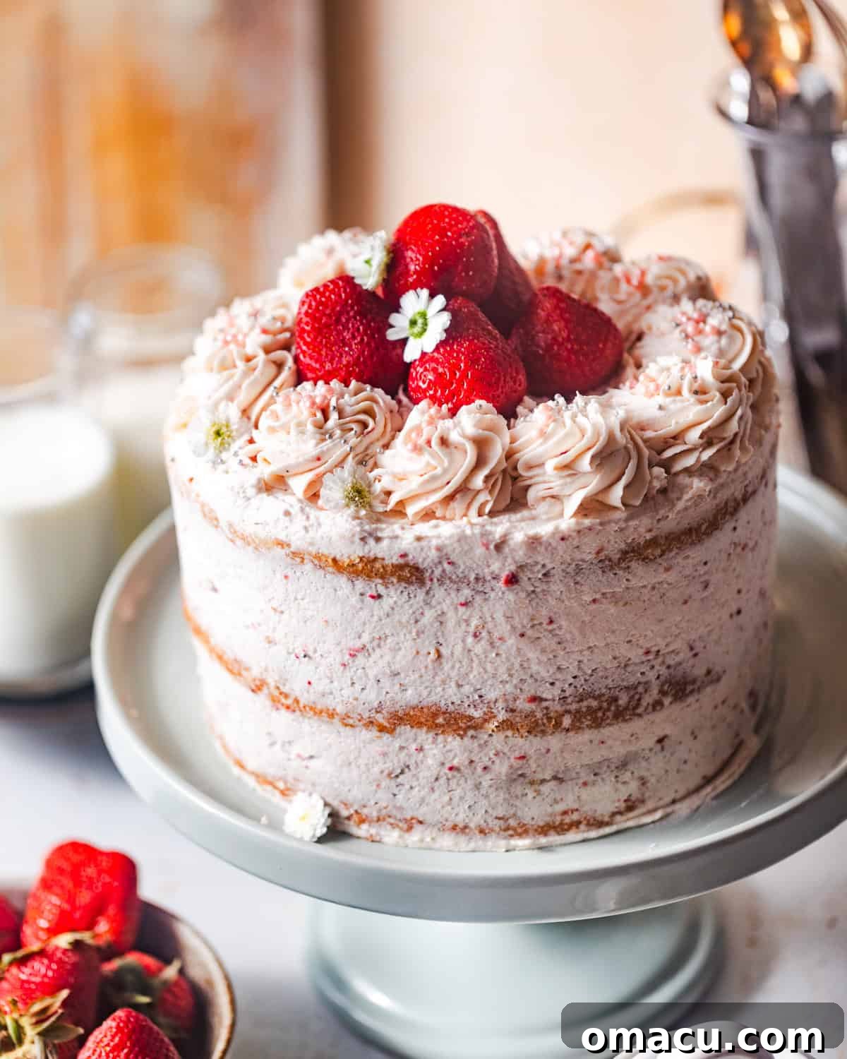 The fully assembled strawberry layer cake on a cake stand, adorned with fresh strawberries and delicate edible flowers.