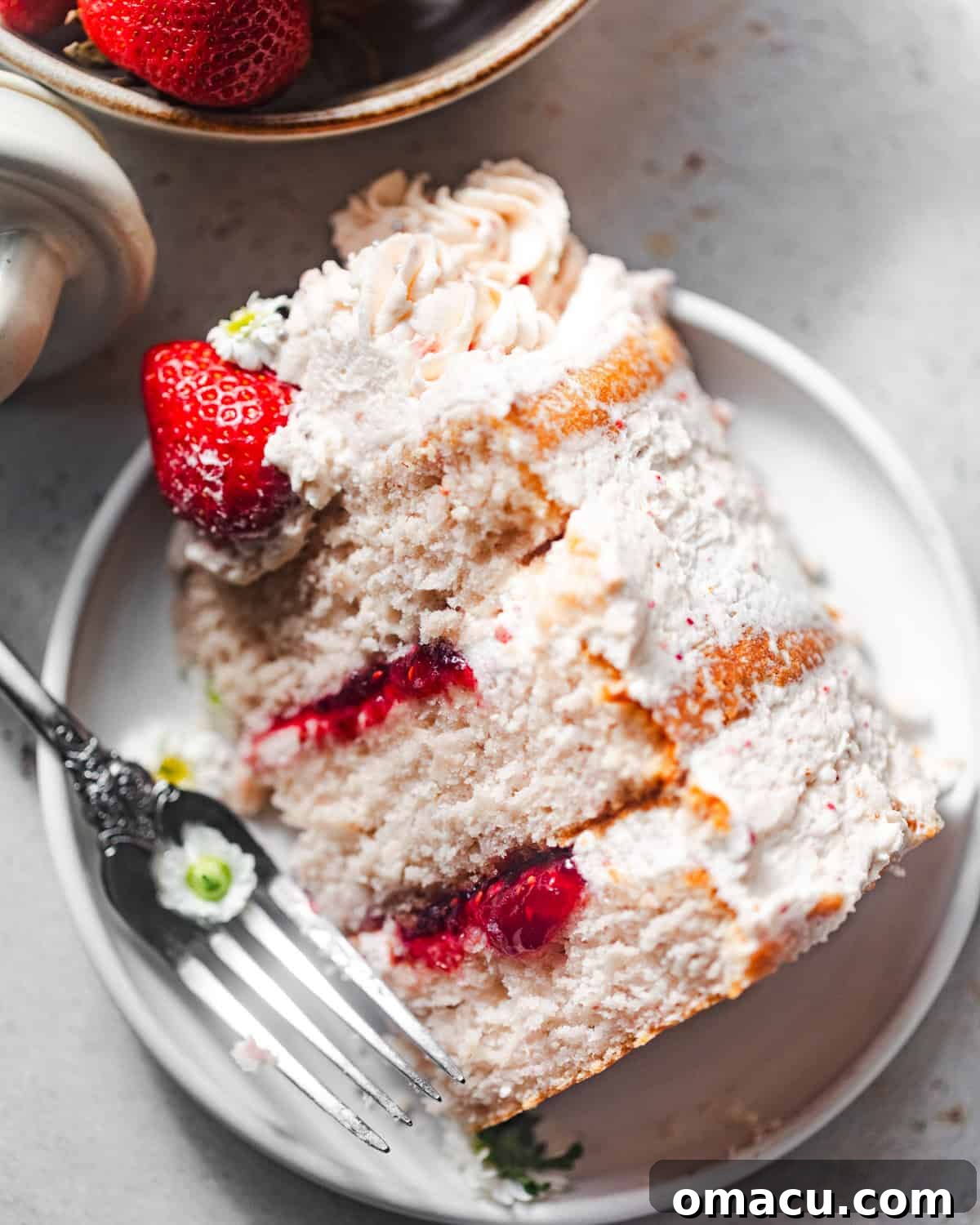 A perfectly sliced piece of strawberry cake on a plate with a fork, showing the vibrant layers and appealing texture.