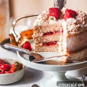 Strawberry cake on a cake stand with a slice cut out of the cake so that you can see the strawberry filling.
