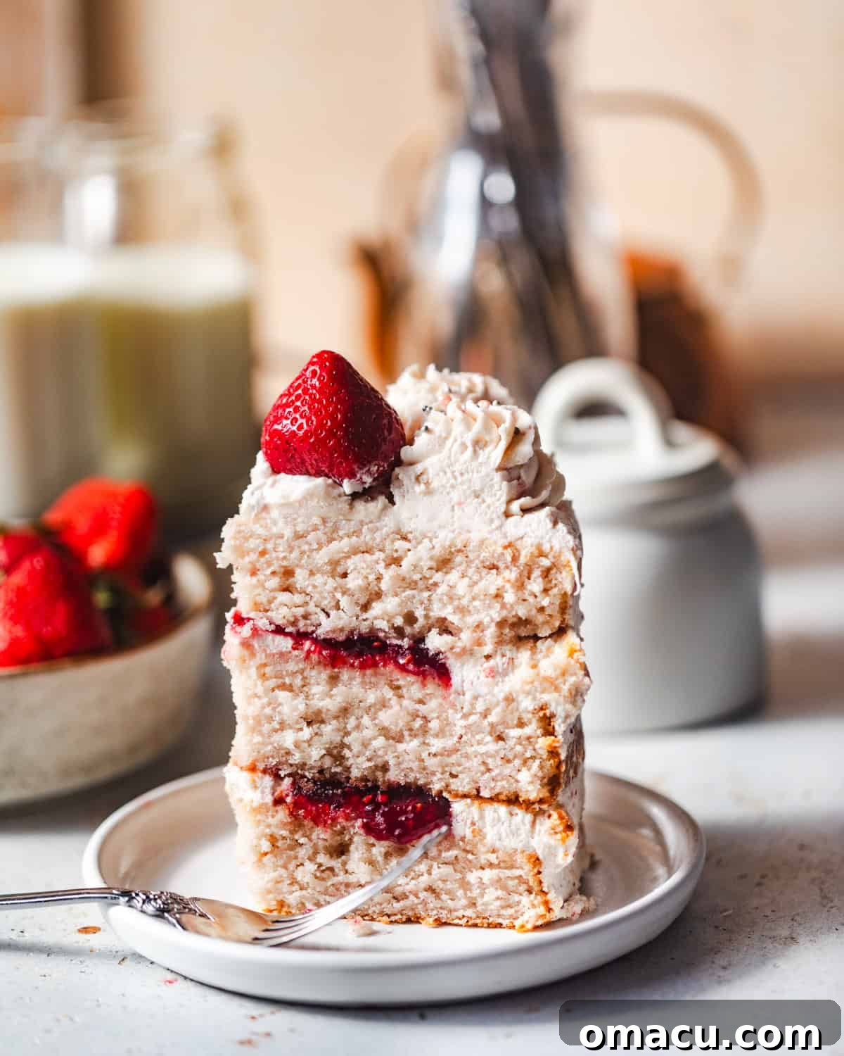 A delicious slice of strawberry cake on a pristine white plate, accompanied by a fork, ready to be enjoyed.