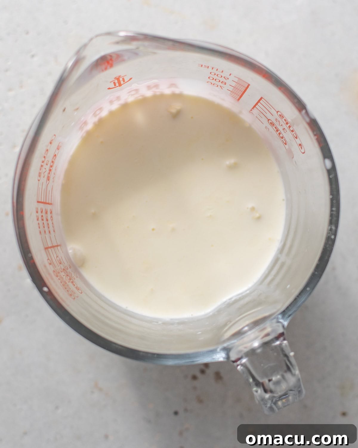 Melted white chocolate and heavy cream in a glass measuring cup, forming a smooth ganache base.