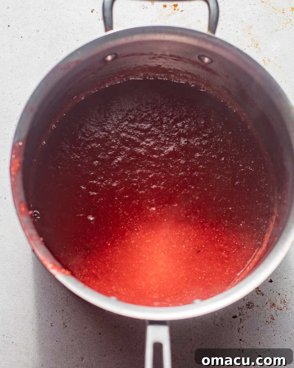 Strawberry puree reducing in a saucepan over medium heat, transforming into a thick, jammy filling.