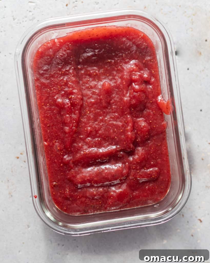 Thick, glossy strawberry jam filling in a bowl, cooling and ready for cake assembly.