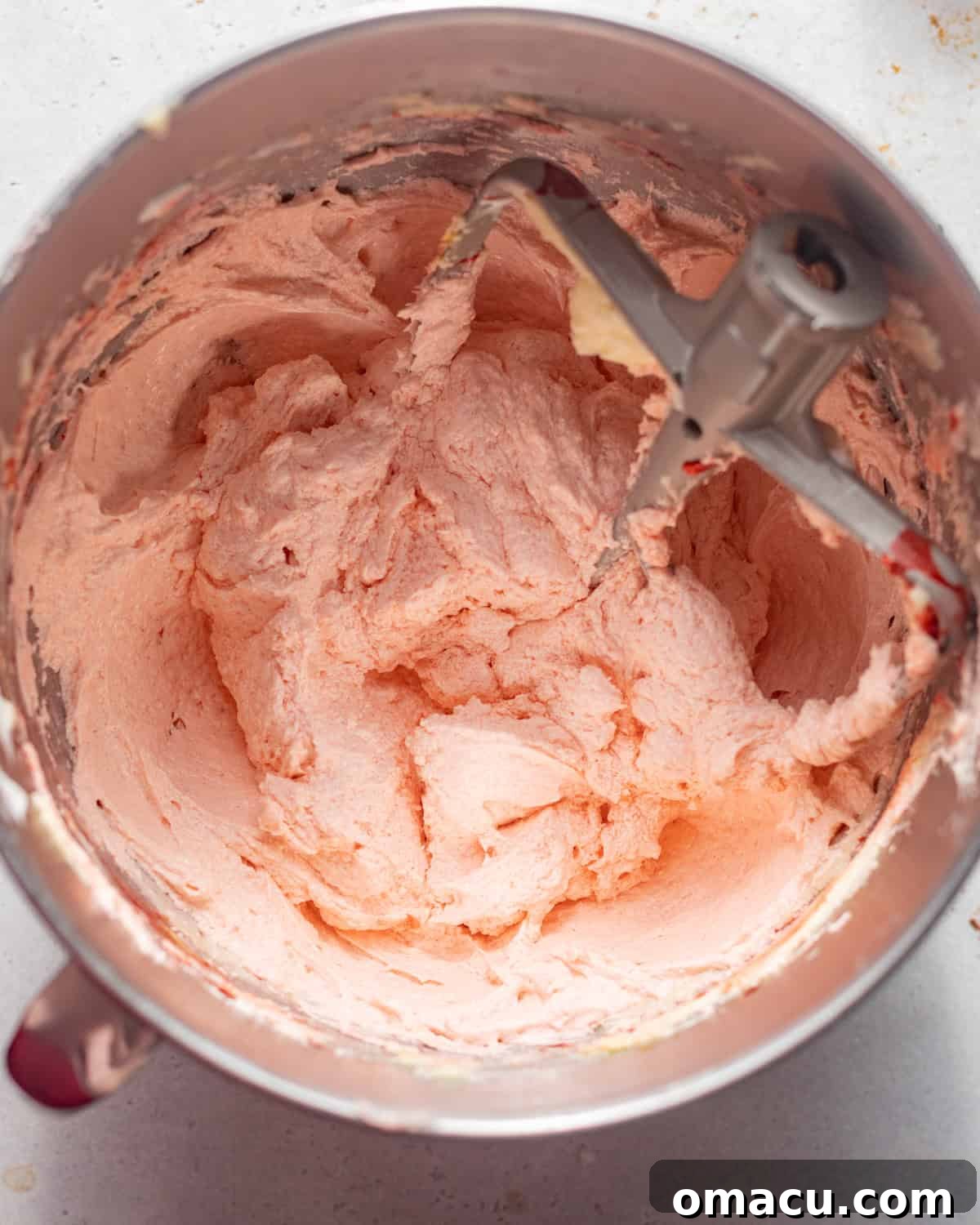 Vibrant pink strawberry cake batter in the bowl of a stand mixer, smooth and ready for baking.