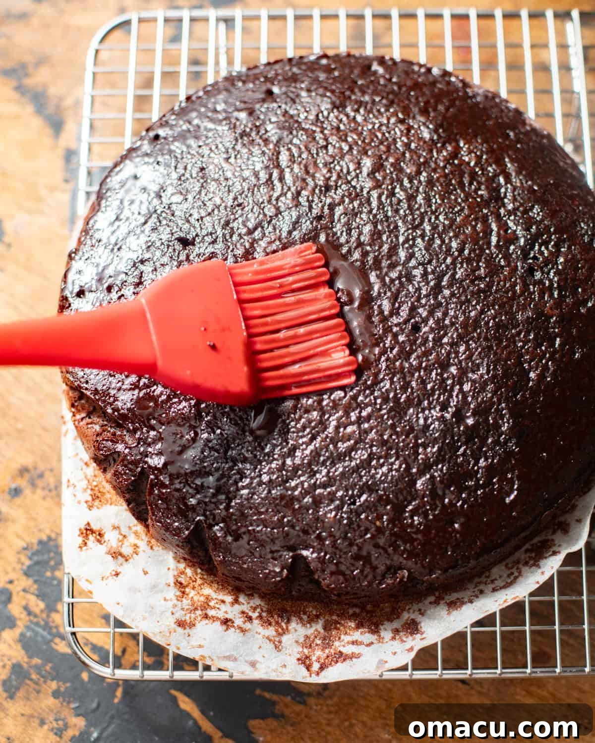 A pastry brush expertly coating the warm chocolate cake layers with a generous application of chocolate syrup.