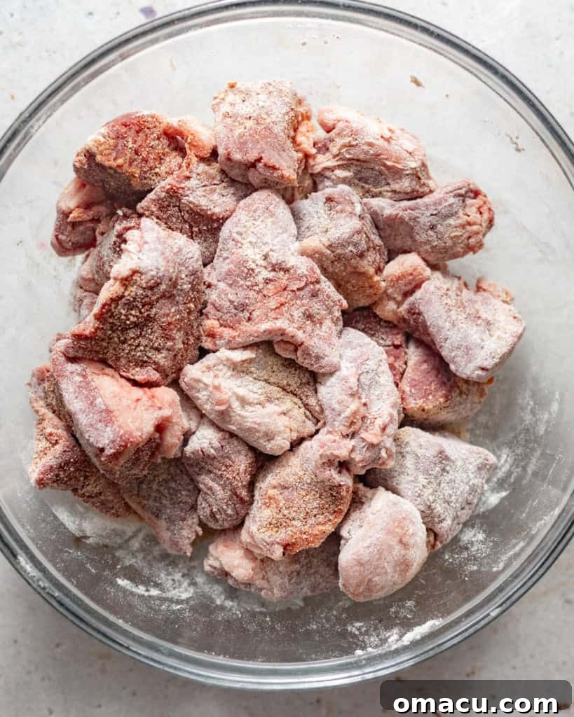 Diced beef chunks in a bowl, evenly coated with seasoning and flour.