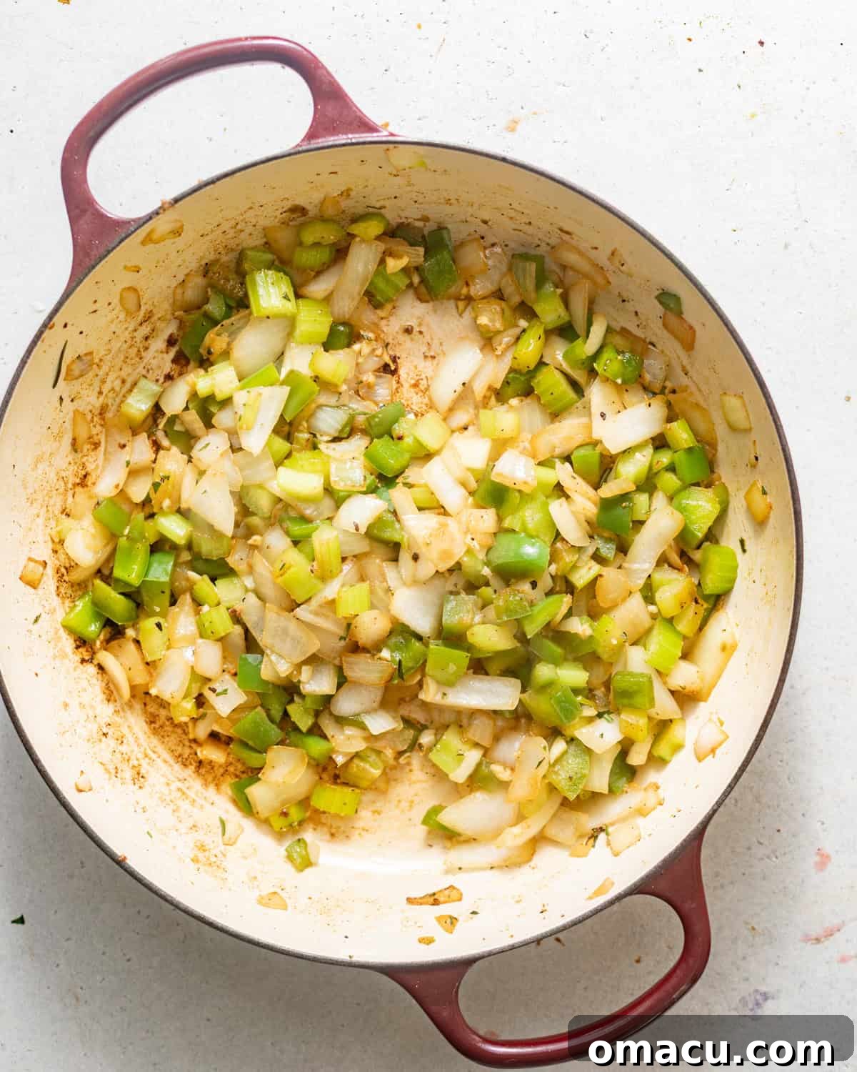 Diced celery, onion, bell pepper, and garlic sautéing in a pot with melted butter.