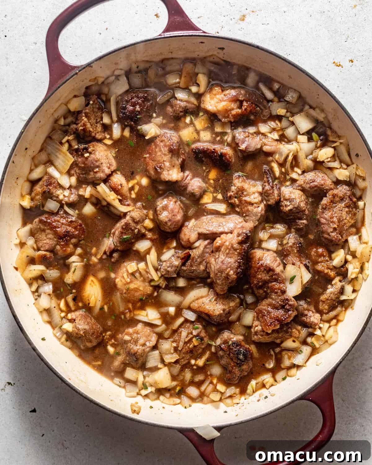 Beef broth, Sazón, and beefy onion mix added to the pot with sautéed aromatics, ready for simmering.