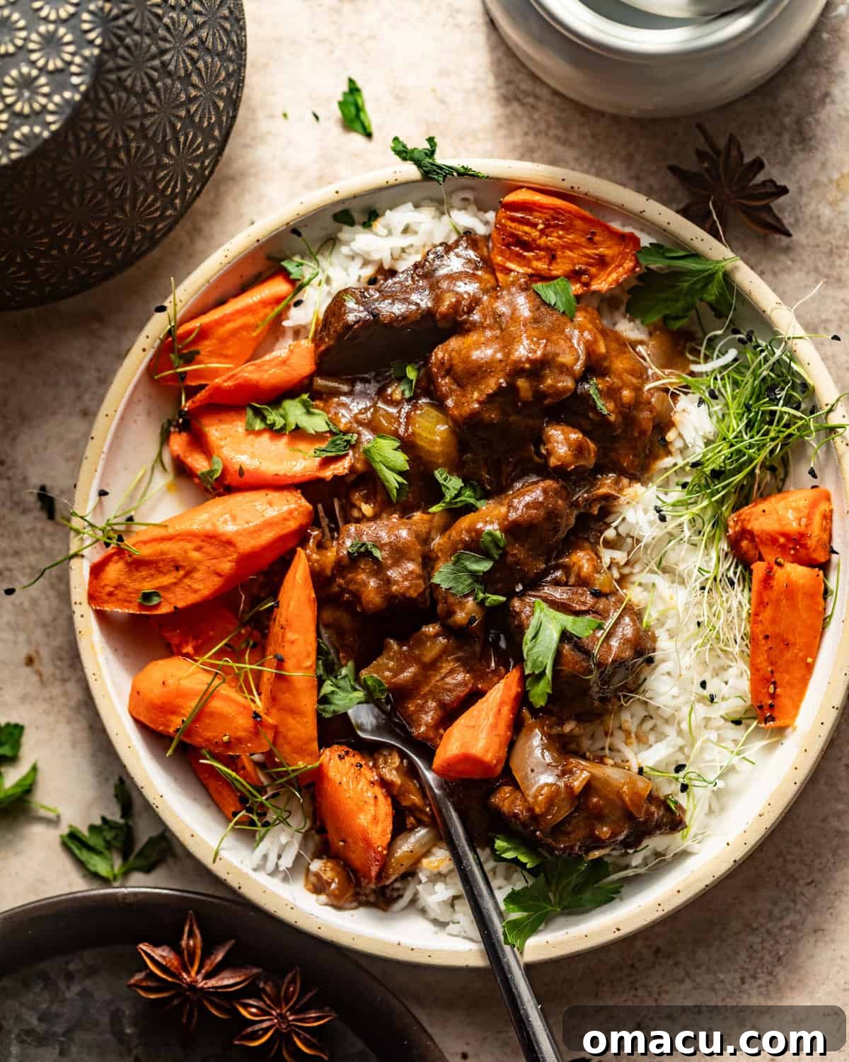 Overhead photo of beef tips and gravy elegantly plated with roasted carrots and fresh parsley as garnish.