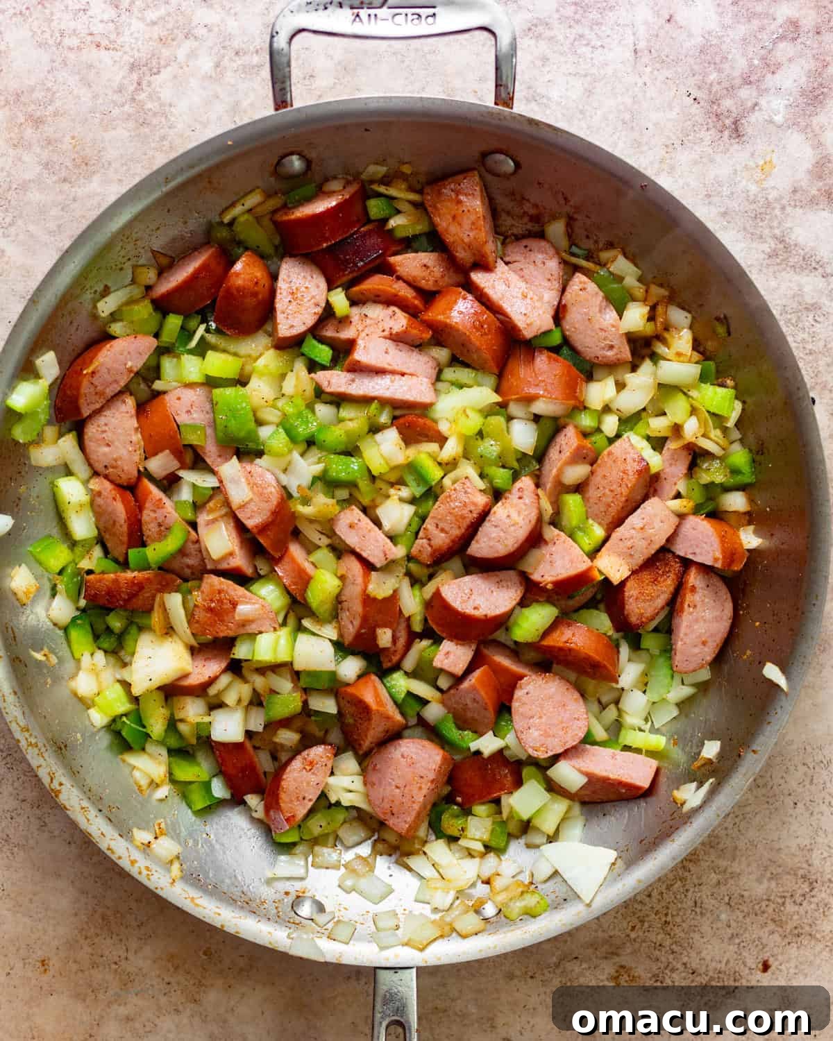 Andouille sausage, diced onion, bell pepper, garlic, and celery cooking together in a skillet, forming the aromatic base of the sauce.