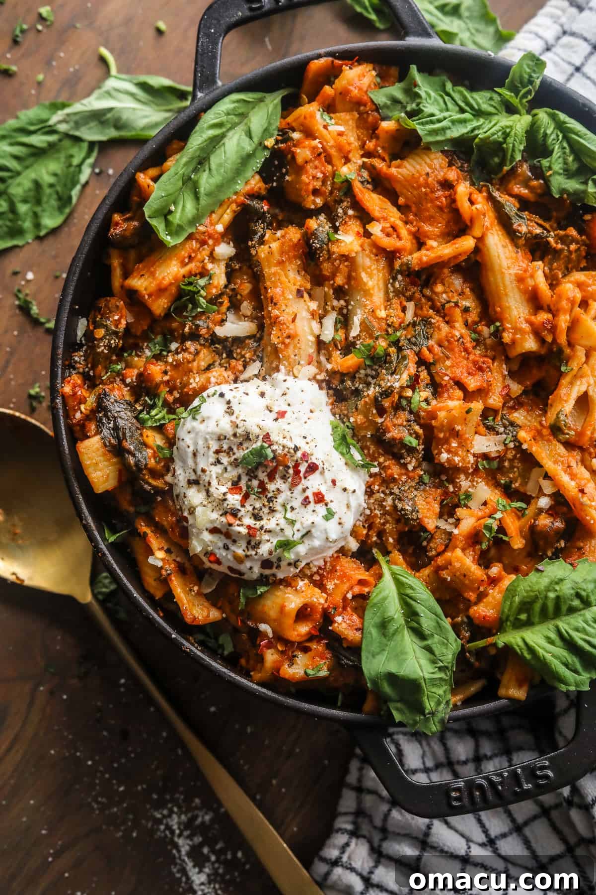 A serving of creamy tomato pasta with a spoon in a rustic pot on a wooden surface.