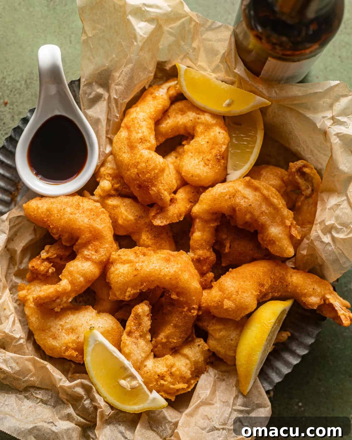 Overhead shot of perfectly golden beer battered shrimp arranged on a round plate, with a small bowl of malt vinegar for dipping.