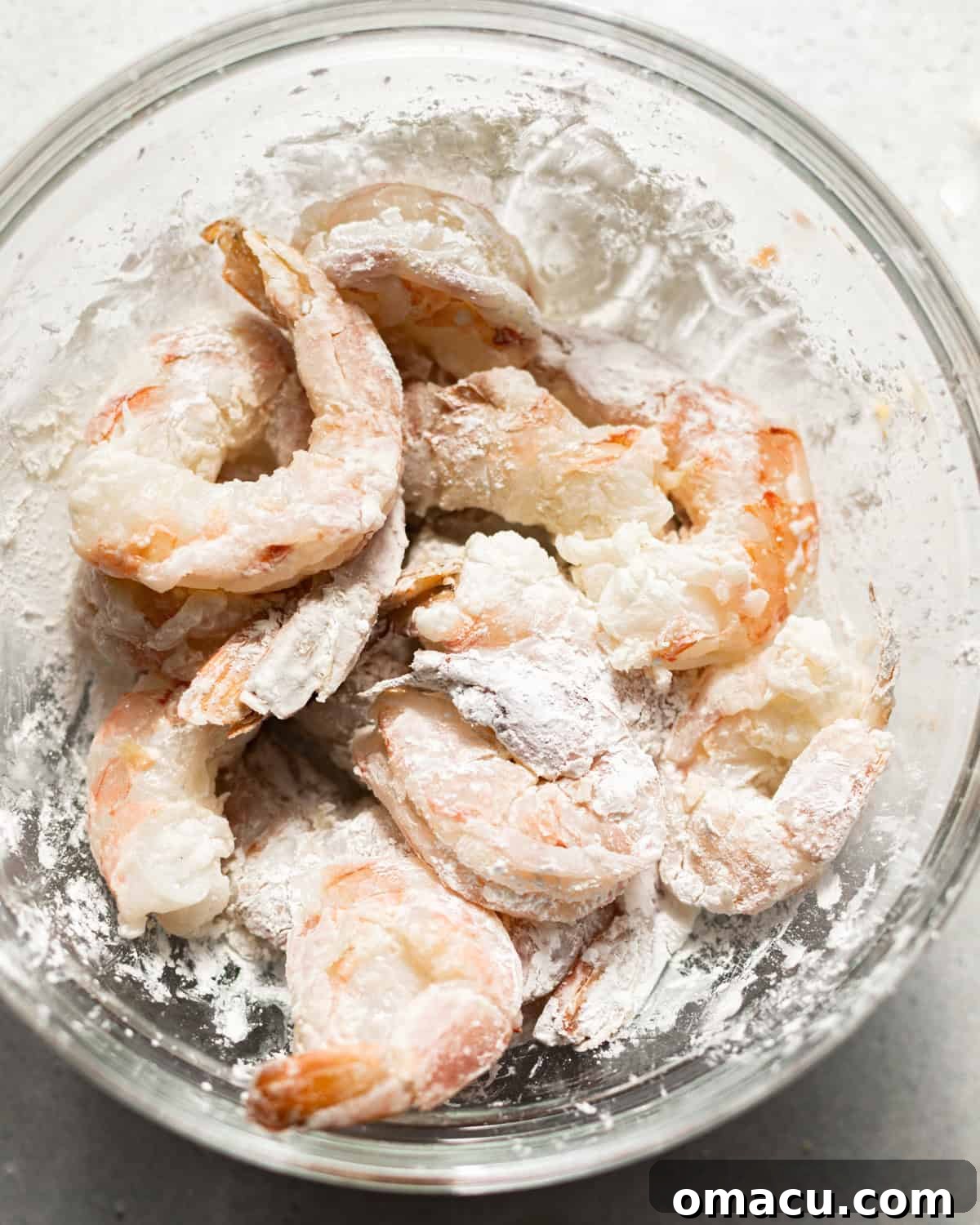Shrimp thoroughly coated in cornstarch in a bowl, prepared for dipping into the beer batter.
