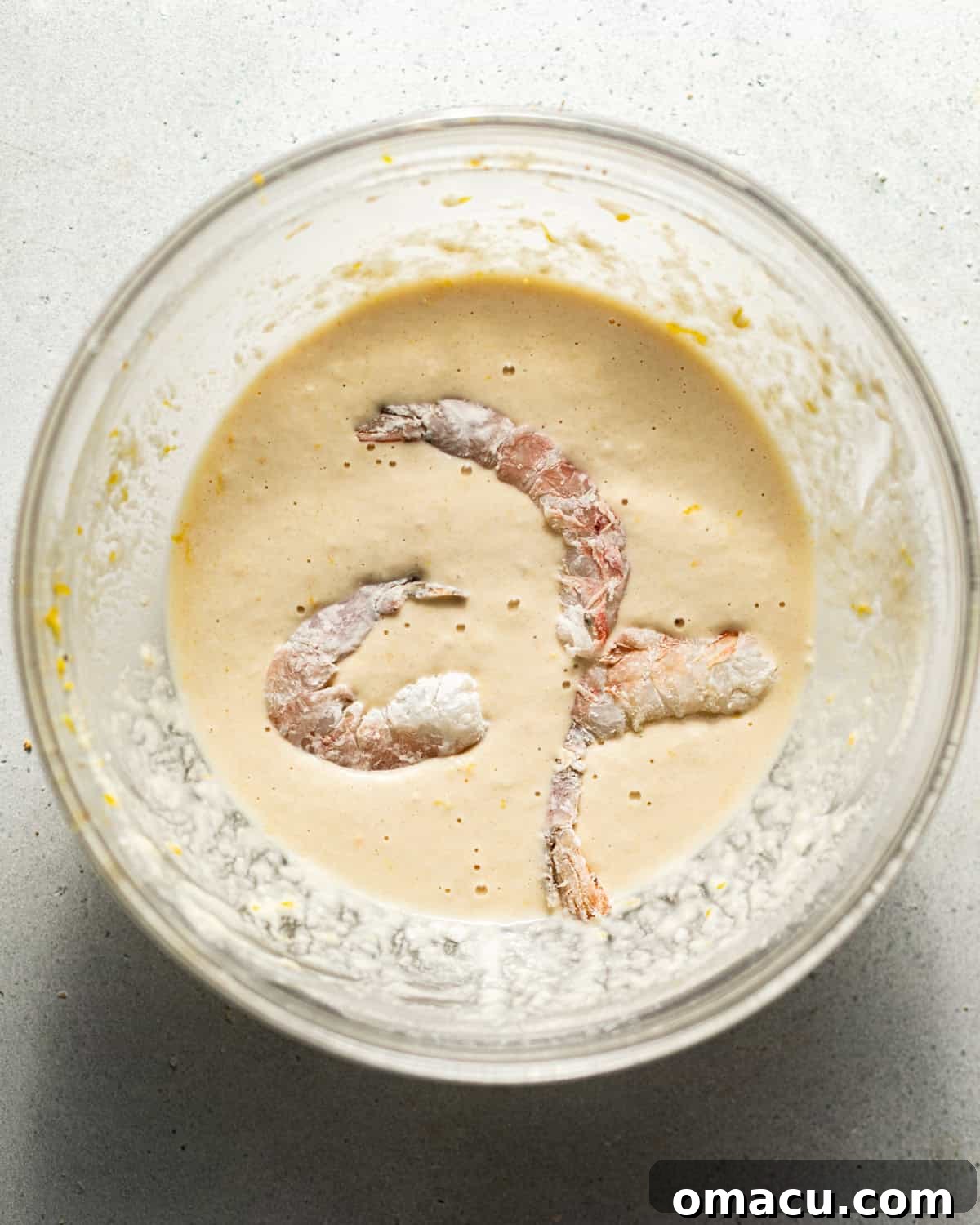 A shrimp being dipped into the prepared beer batter, showing a generous coating before frying.