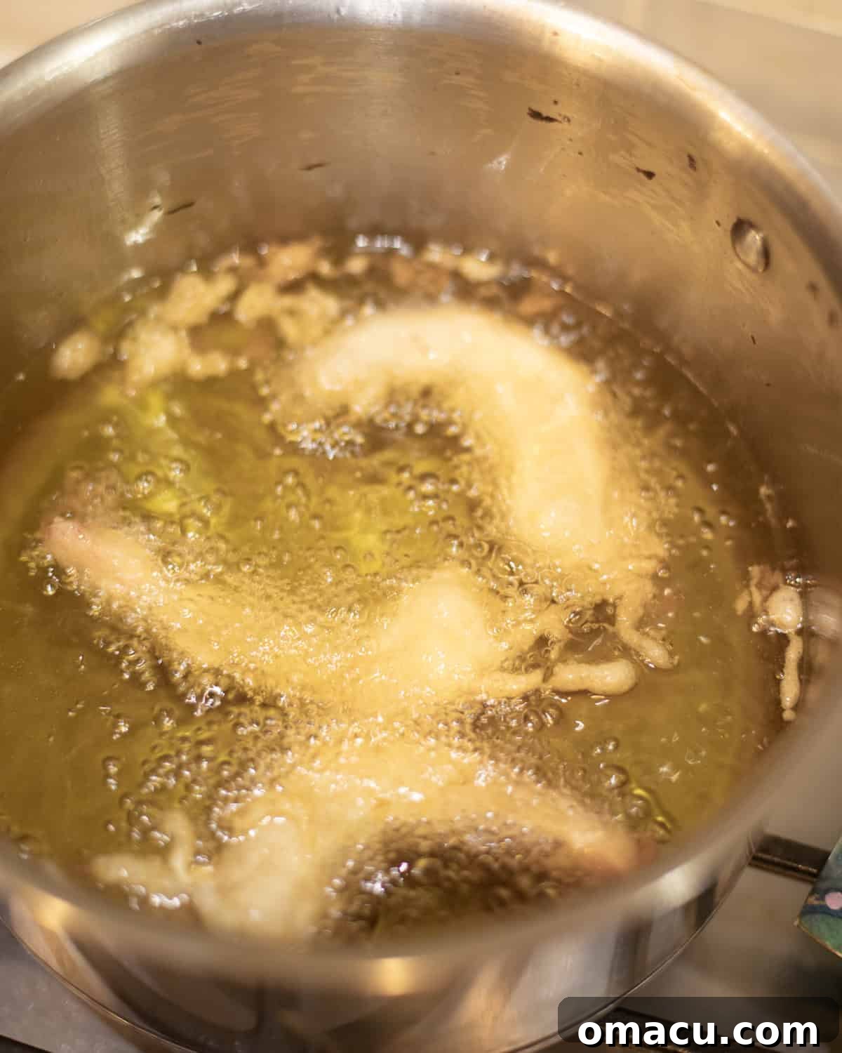 Several beer battered shrimp frying in hot oil in a heavy bottom pan, achieving a golden brown color.