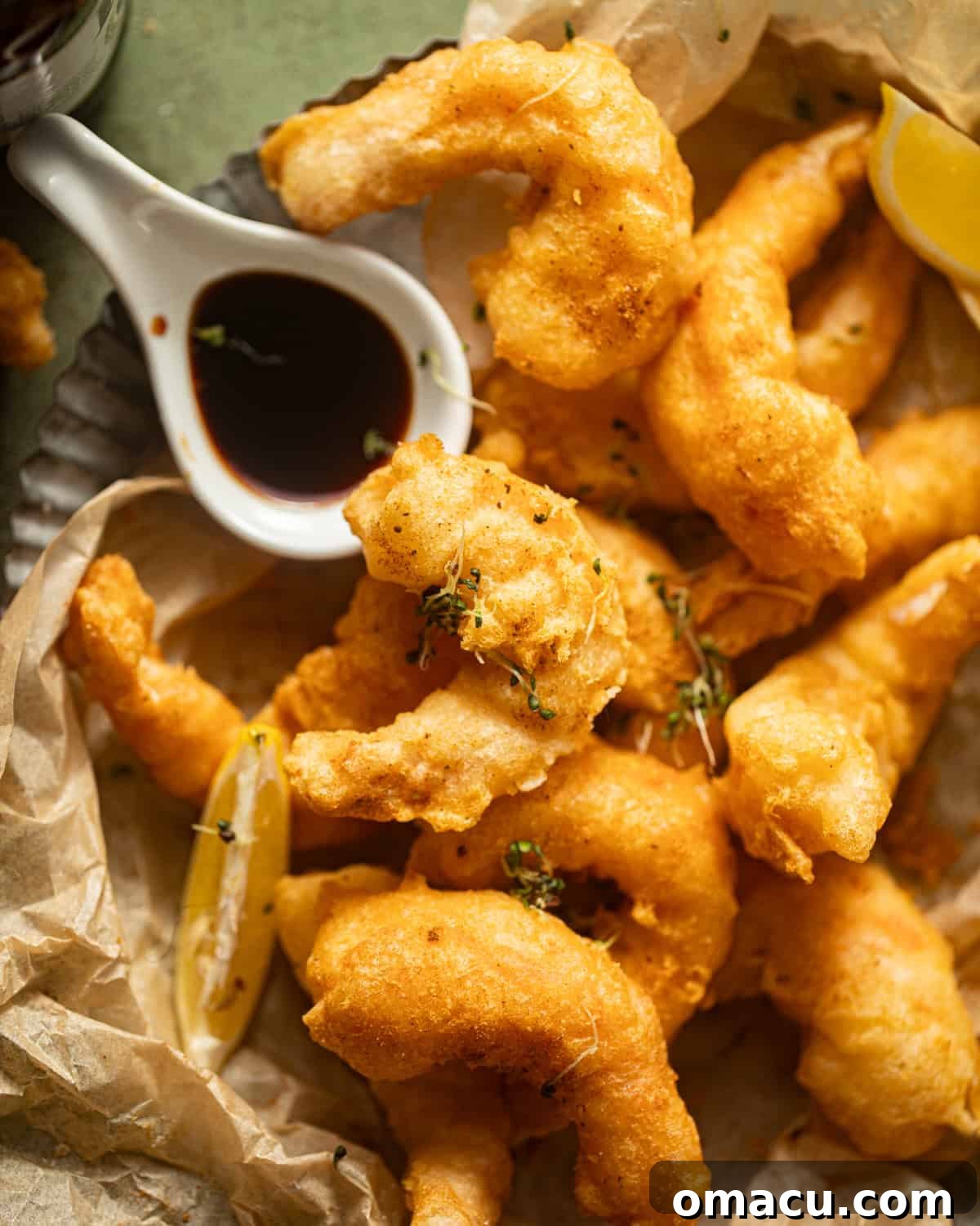 Freshly fried beer battered shrimp resting on parchment paper with a lemon wedge, sprinkled with additional Old Bay seasoning.