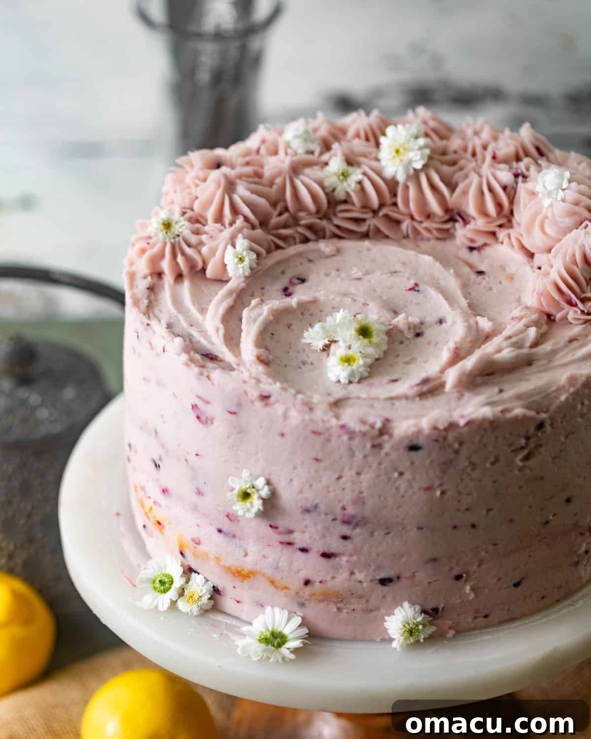 A fully frosted Lemon Blackberry Cake on a cake stand, garnished with fresh blackberries.