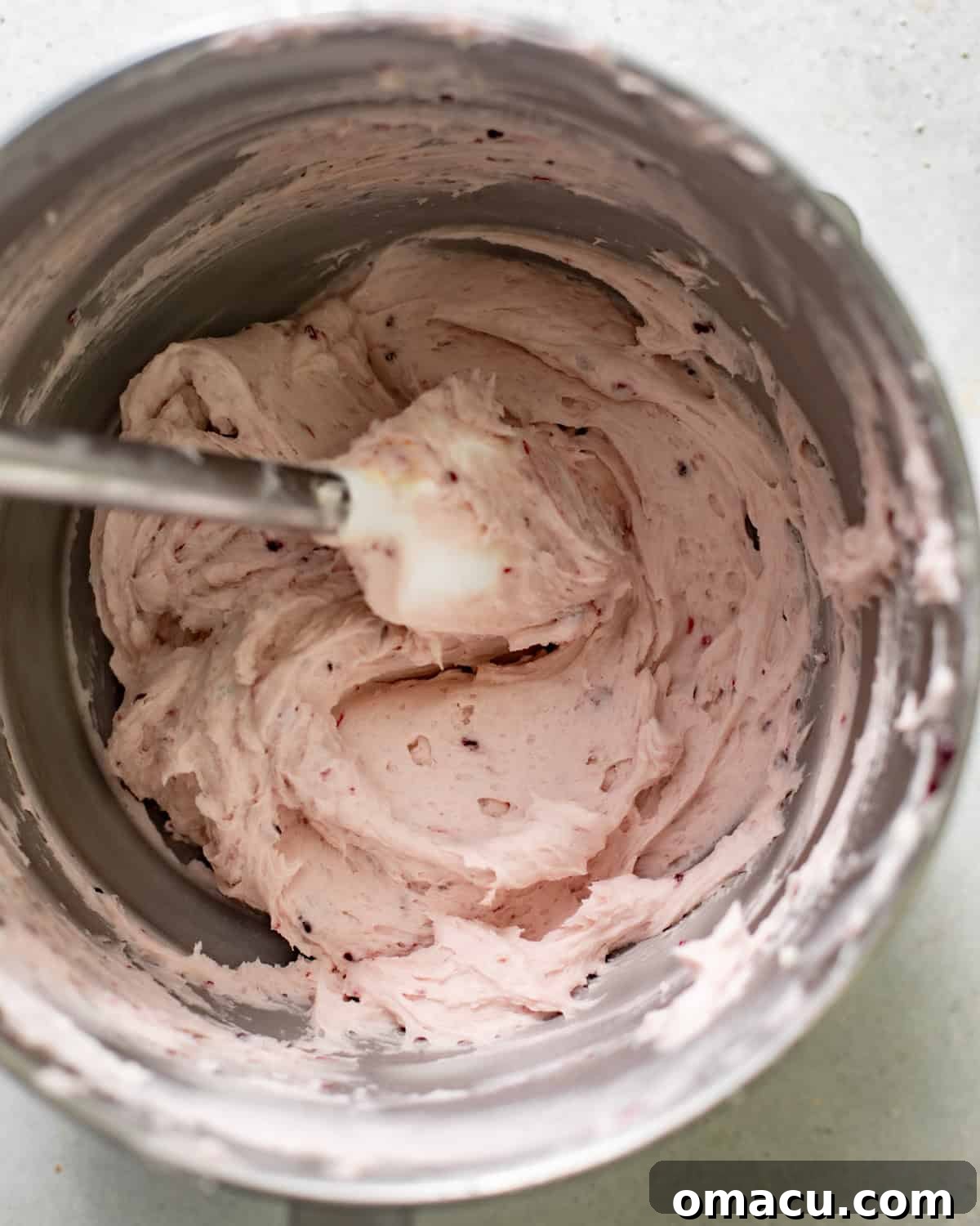 Smooth and fluffy blackberry mascarpone frosting in a mixing bowl with a spatula.