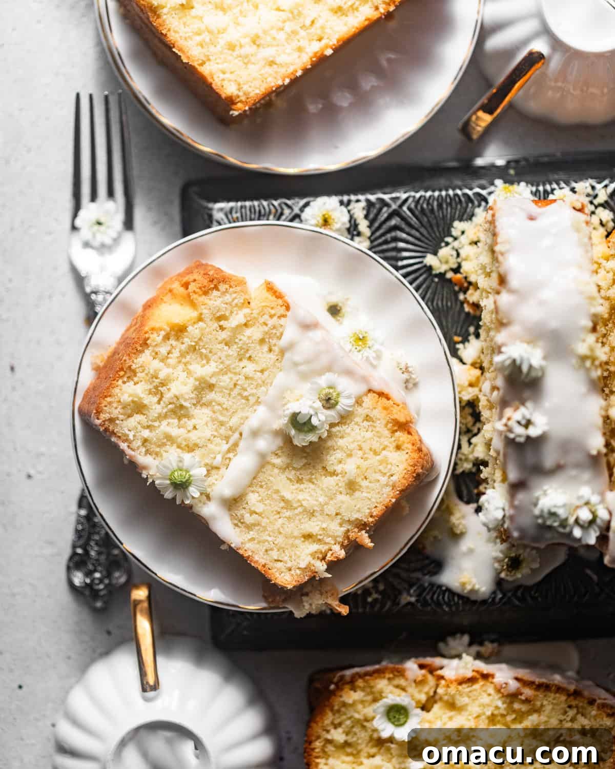 A perfectly sliced piece of moist coconut loaf cake on a pristine white plate, generously coated in a glistening coconut glaze and elegantly garnished with delicate edible flowers, showcasing its inviting texture.