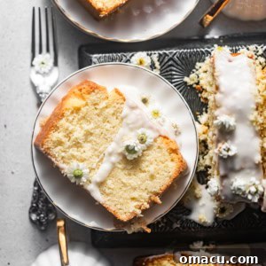 A delightful slice of coconut loaf cake presented on a serving plate, adorned with a smooth coconut glaze and fresh edible flowers.